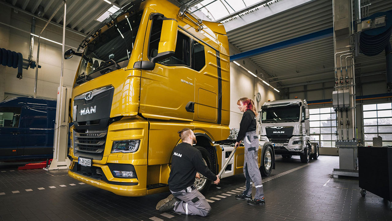 Zwei junge Personen in Arbeitskleidung vor einem MAN Truck