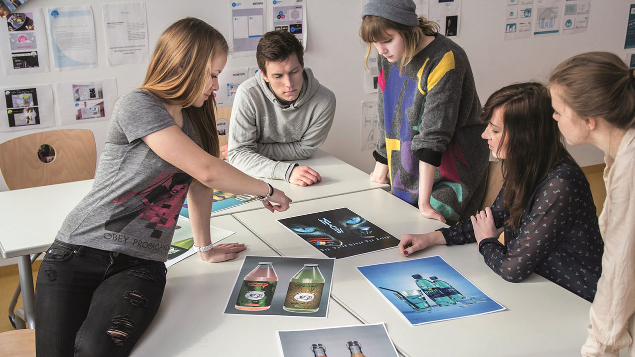 Personengruppe sitzt um einen Tisch und zeigen auf verschiedene Bilder und Grafiken.