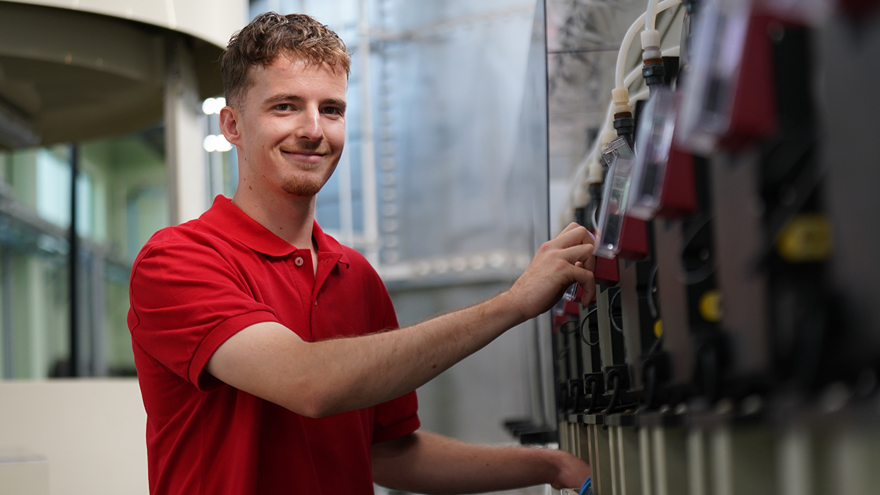 Junger Mensch steht an einer Maschine und lacht in die Kamera