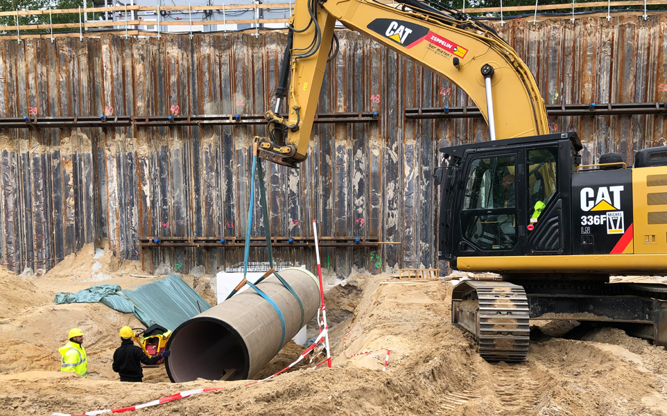 Ein Bagger setzt ein großes Rohr in den Boden ein. 