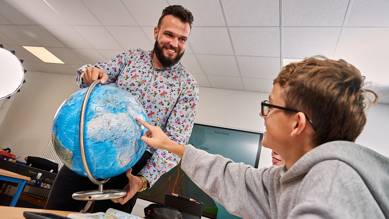 Junge Person zeigt auf einen Globus, den eine andere Person in der Hand hält
