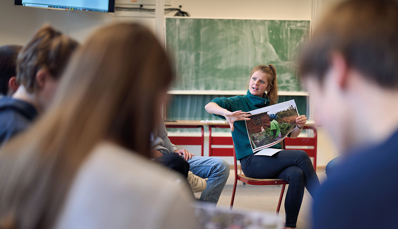 Jüngere Dame erklärt im Stuhlkreis sitzend ein großes Foto.