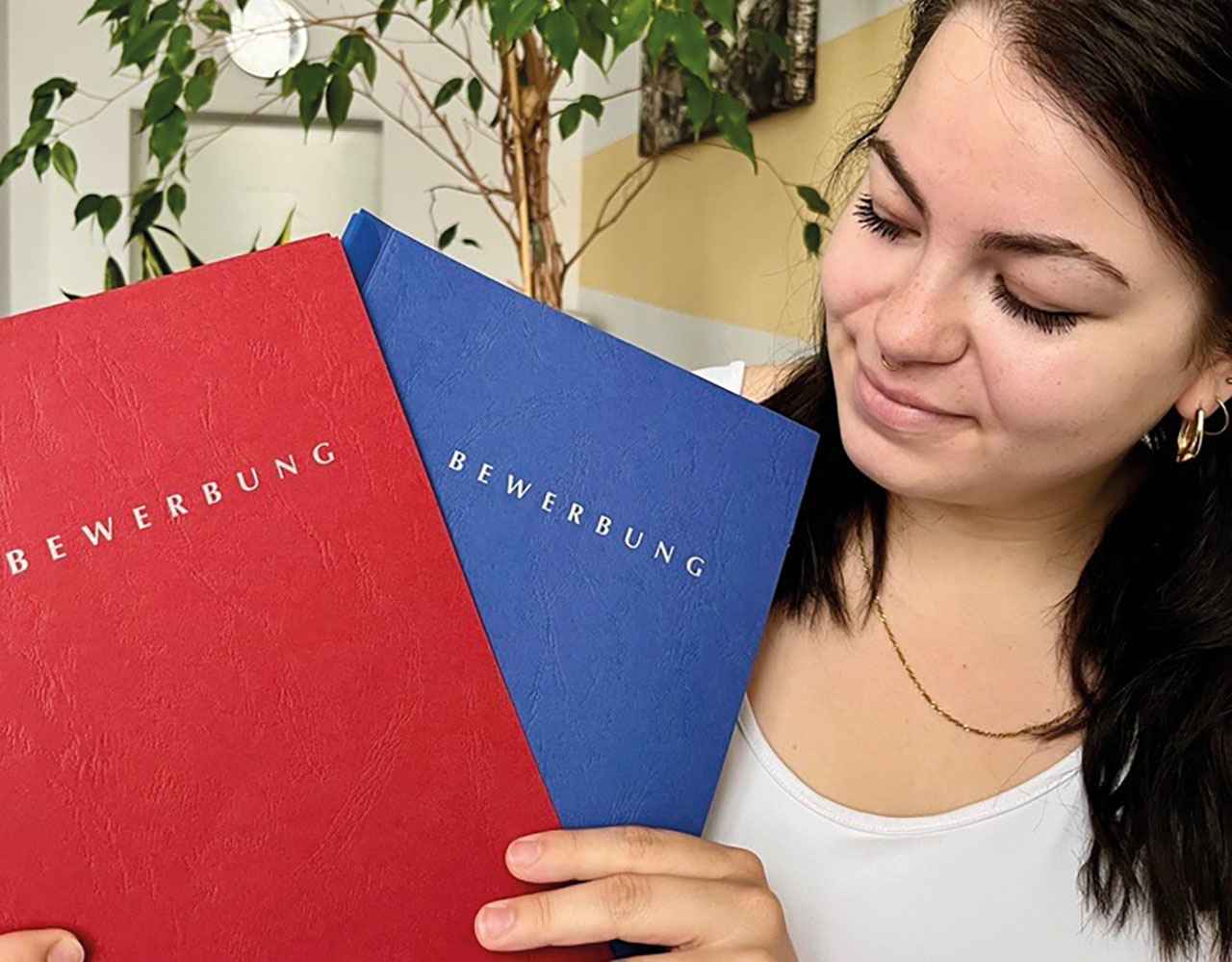 Junges Mädchen halt eine rote und eine blaue Bewerbungsmappe in die Kamera.