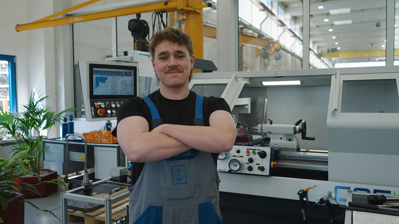 Junge Person in der Produktionsstätte hat die Arme vor der Brust verschränkt und lächelt in die Kamera