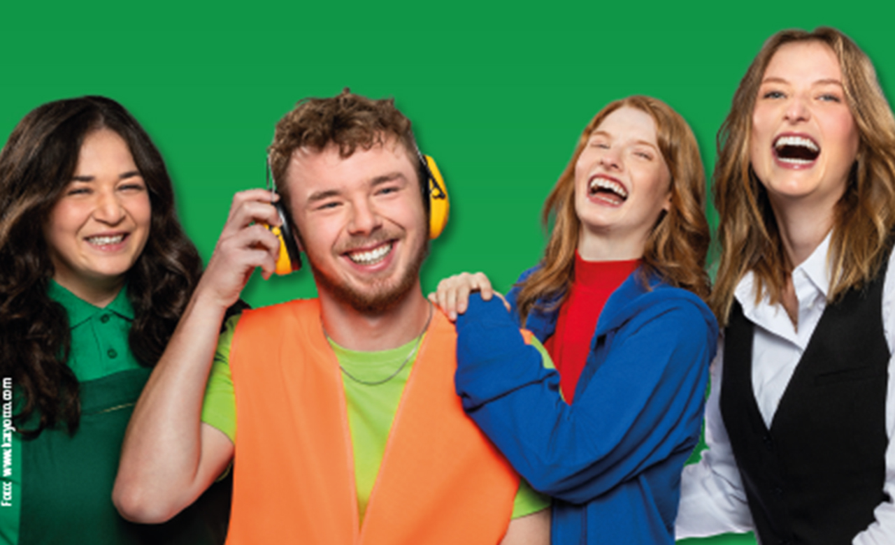 Gruppe junger Menschen vor grünem Hintergrund, alle lachen in die Kamera