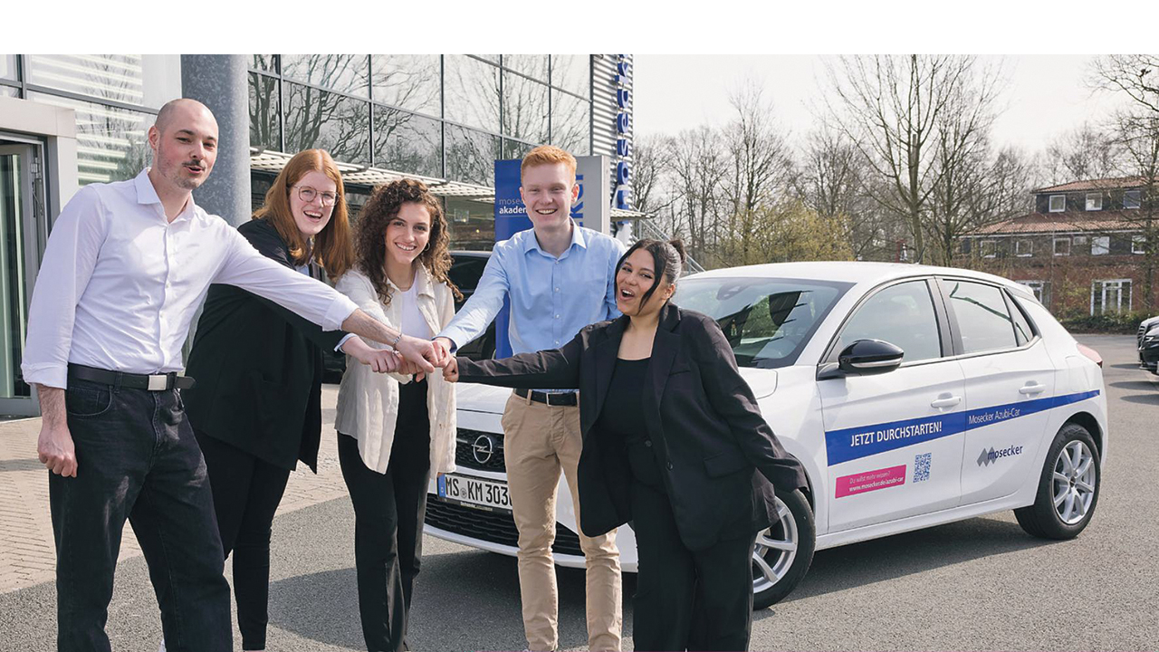 5 junge Mitarbeitende vor einem Firmenwagen beim Team-Fist-Bump.