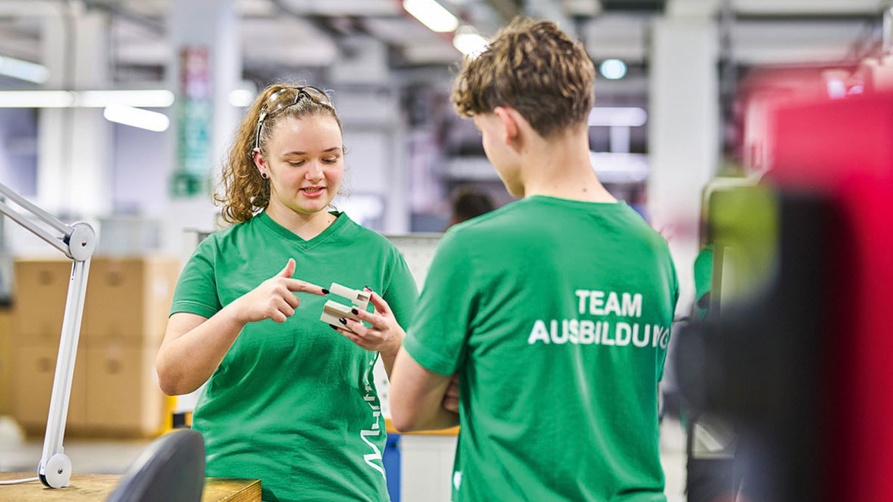 Zwei junge Menschen in grünen T-Shirts mit der Aufschrift "Team Ausbildung" im Gespräch