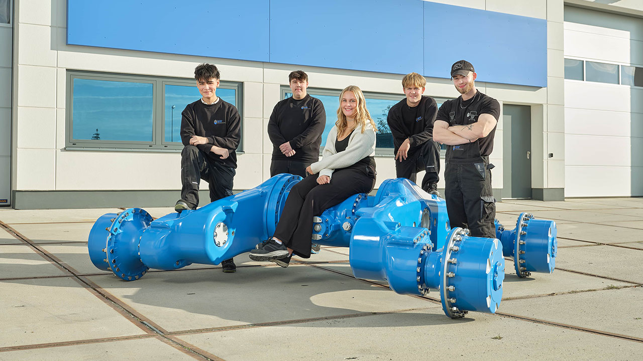 Personengruppe sitzt beziehugsweise steht bei einem hellblauen großen Rohrsystem.