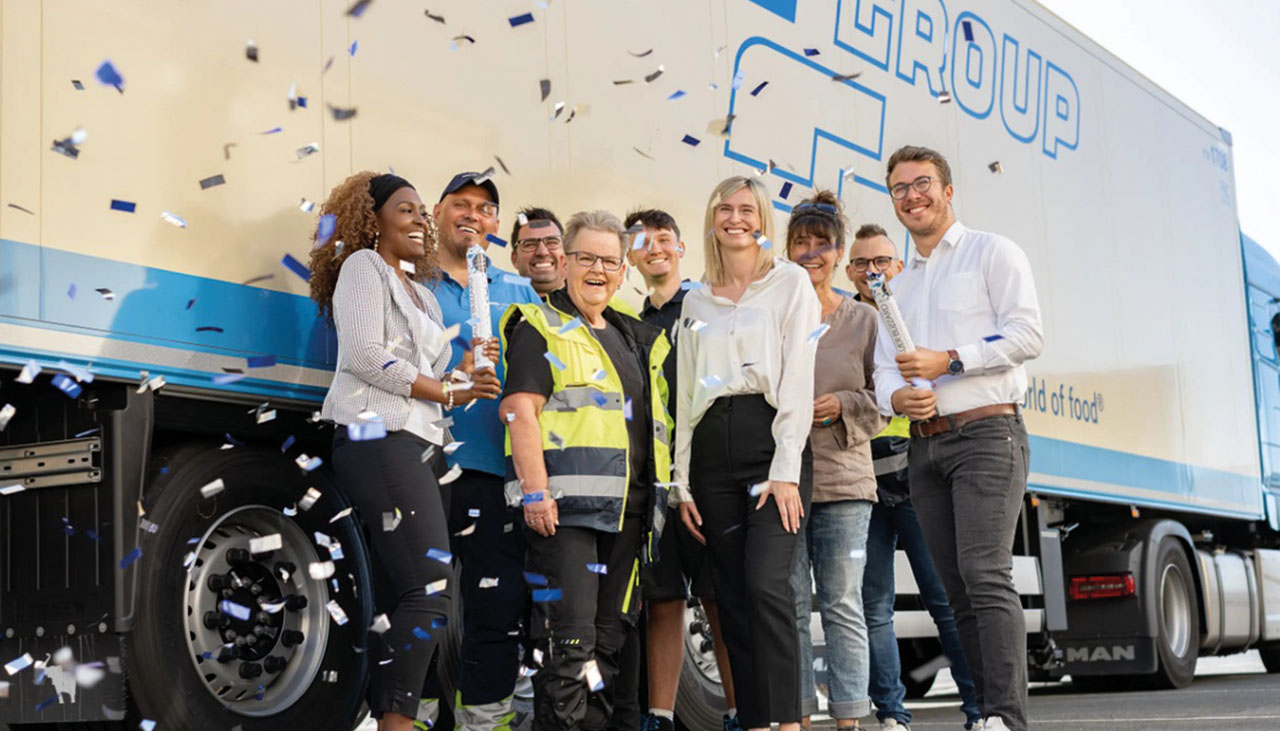 Mitarbeiter stehen vor einem LKW von Nagel-Group Logistics. Es fliegen große bunte Konfettis.
