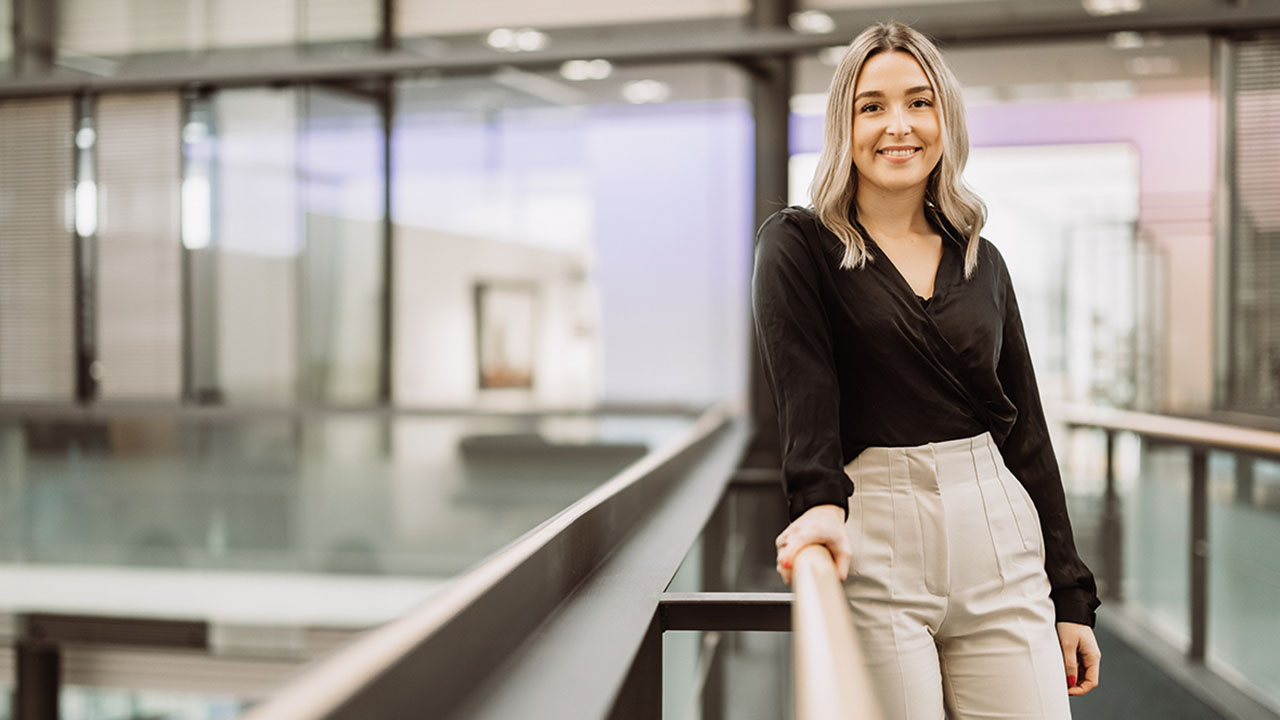 Junge lächelnde Perosn mit mittellangen Haaren im Bankgebäude