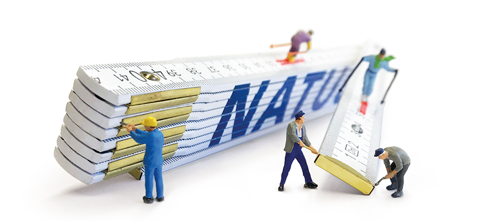 Kleine Plastikmännchen halten und arbeiten an einem großen Gliedermaßstab (Zollstock).