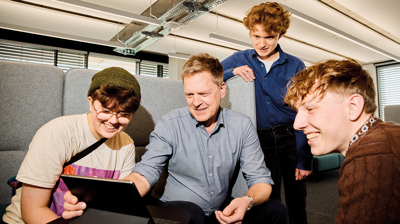 Kleine Gruppe Mitarbeitender in einer Sitzgruppe vor dem Laptop fröhlich in der Gruppe sprechend.