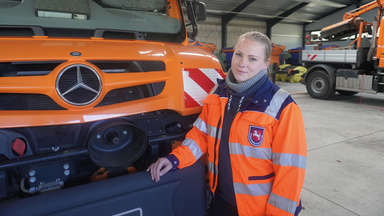 Frau in Arbeitskleidung vor orangenem LKW
