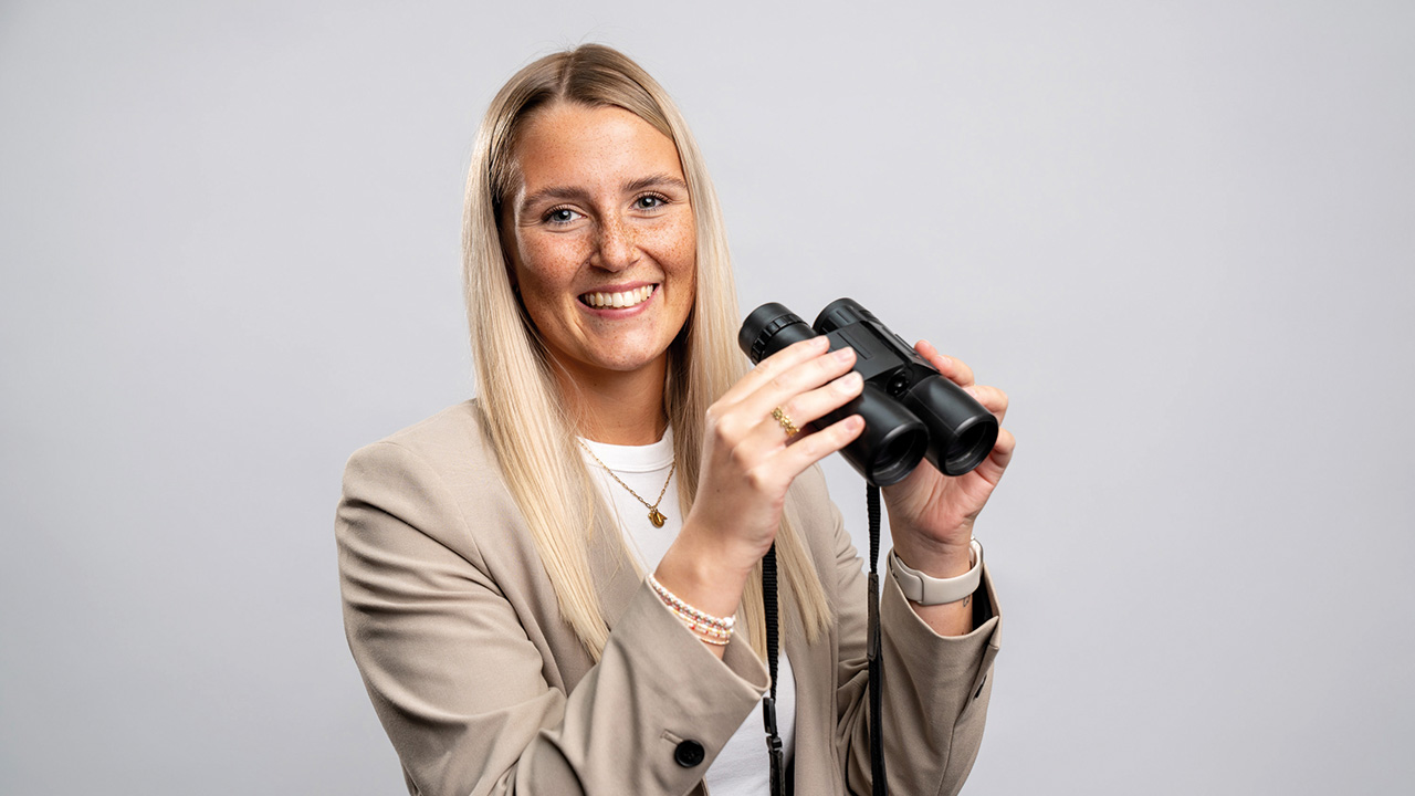 Junge Frau mit Fernglas, lächelt in die Kamera