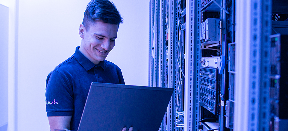 Azubi am Laptop vor Schaltzentrale