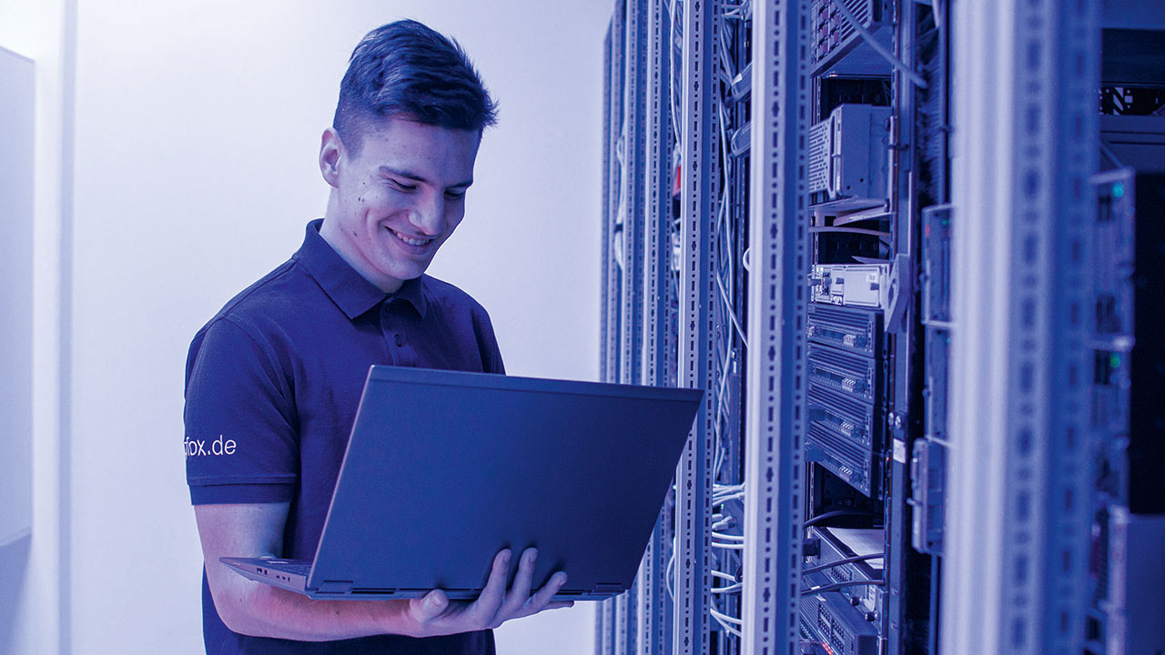 Azubi am Laptop vor Schaltzentrale