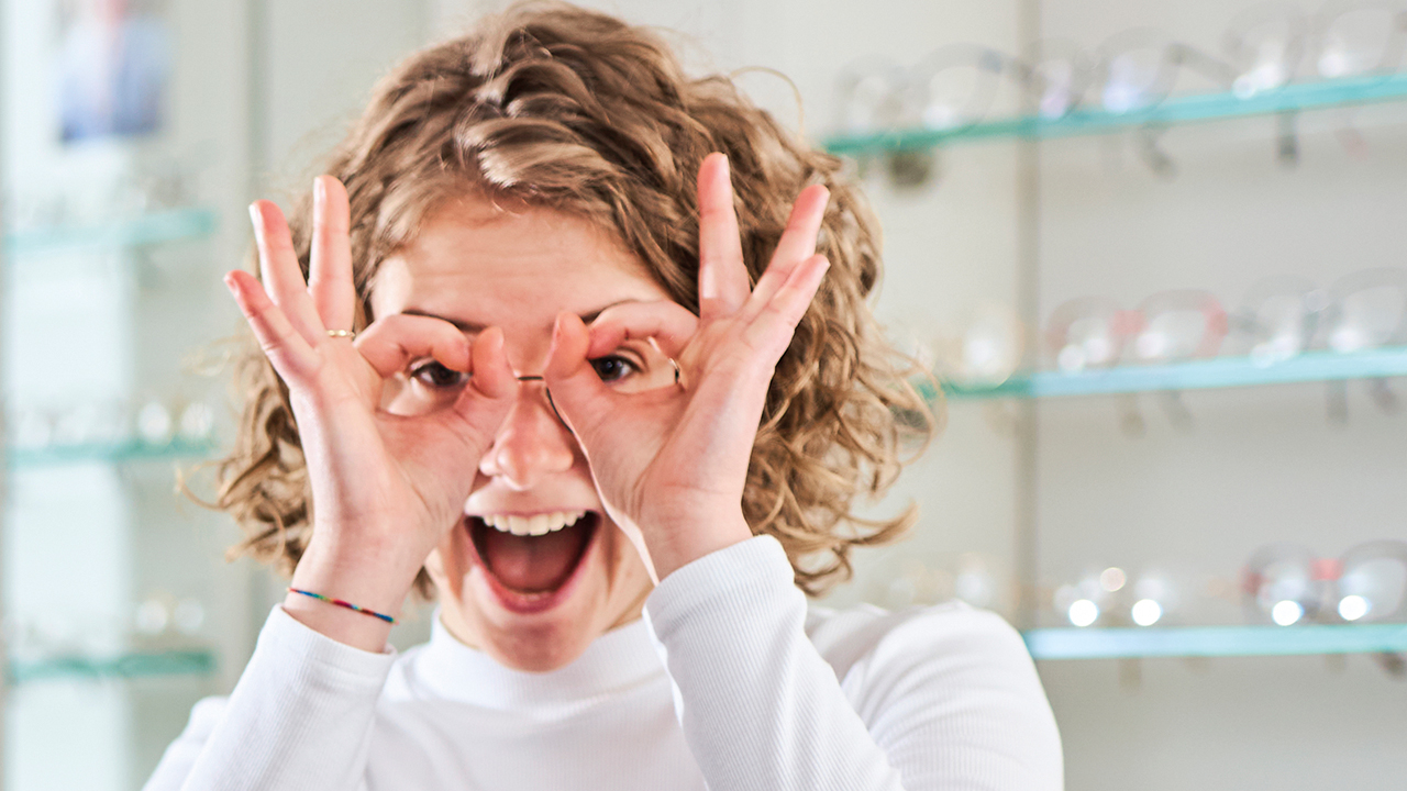 Junge Person die Daumen und Zeigefinger beider Hände zu Kreisen formt und durchschaut.