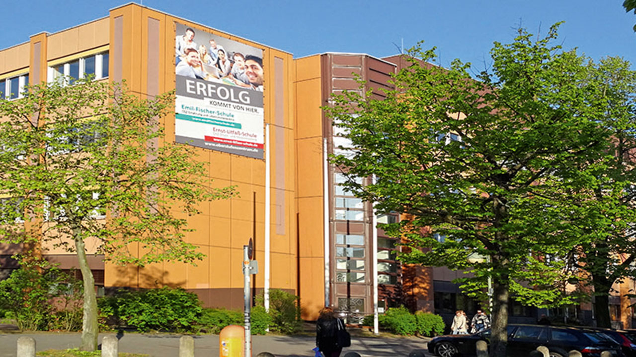Das Gebäude der Emil-Fischer-Schule im Sonnenschein mit grünen Bäumen davor