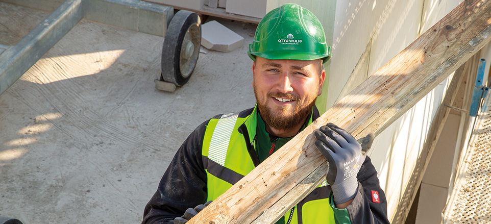 Person trägt Balken auf der Schulter und lächelt in die Kamera.