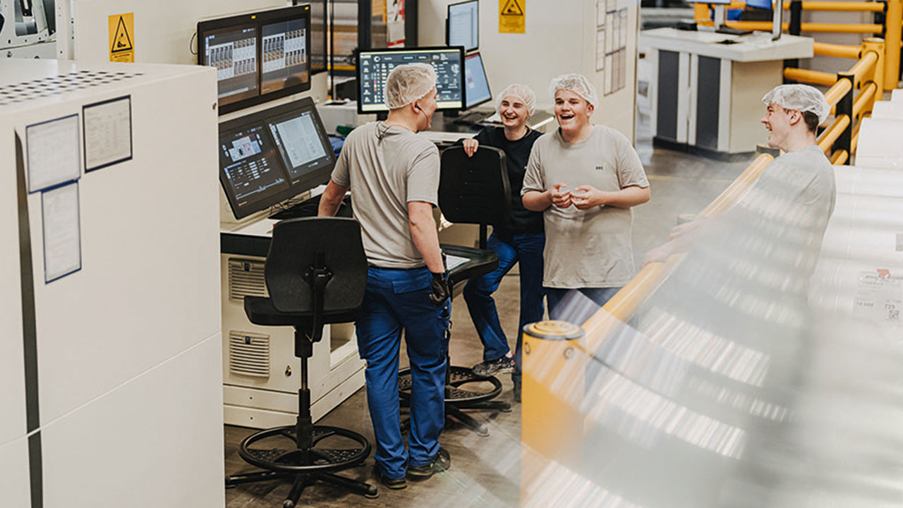 Vier junge Menschen mit Schutzhauben im Gespräch in der Produktionsstätte