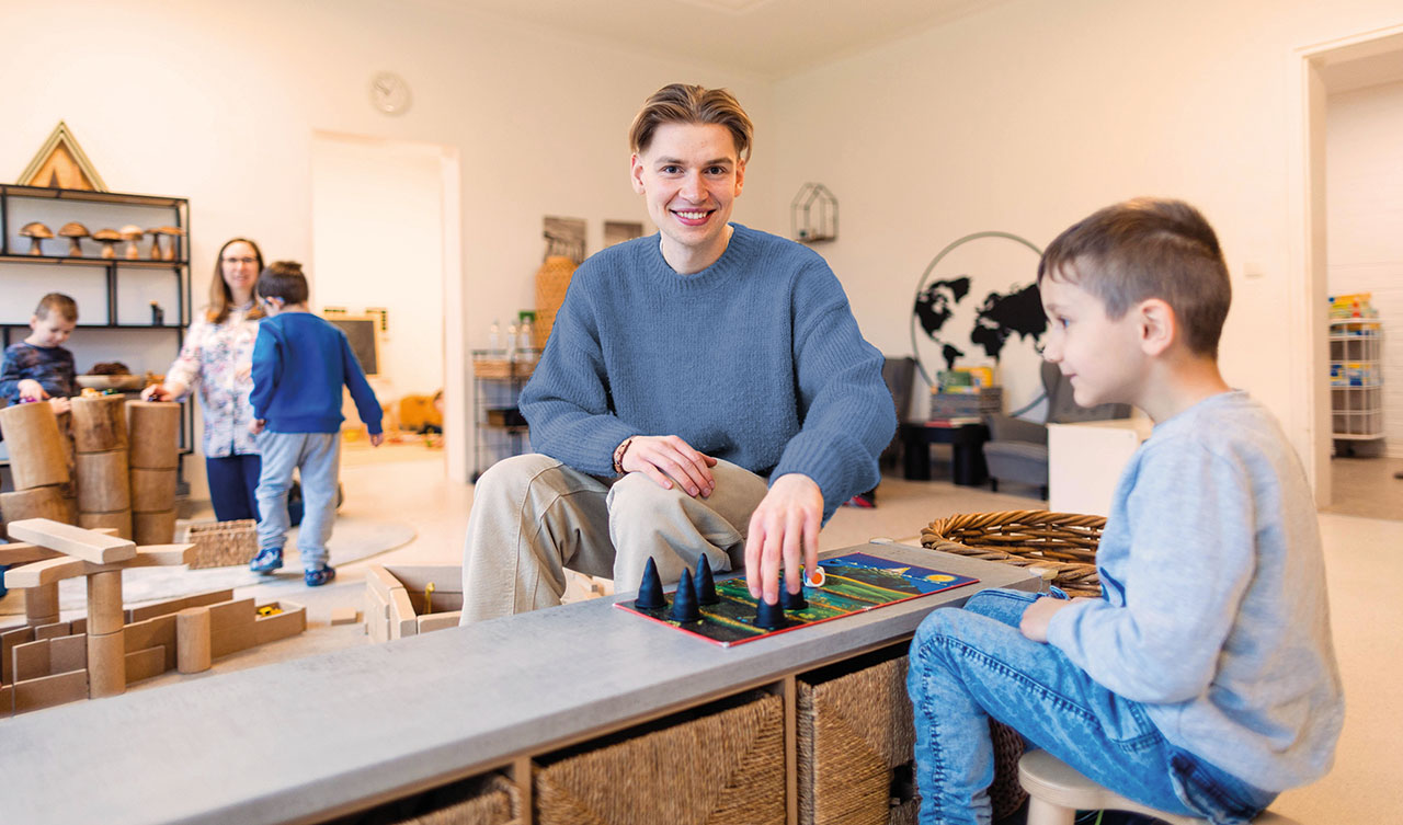 Junger Mann und Kind spielen ein Brettspiel in einer Kindereinrichtung.