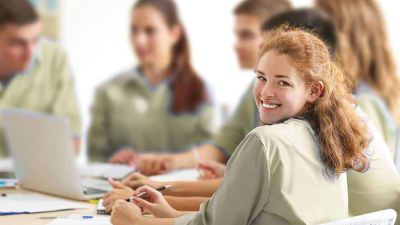 Junge Dame sitzt an einem Tisch und lächelt über die Schulter in die Kamera.