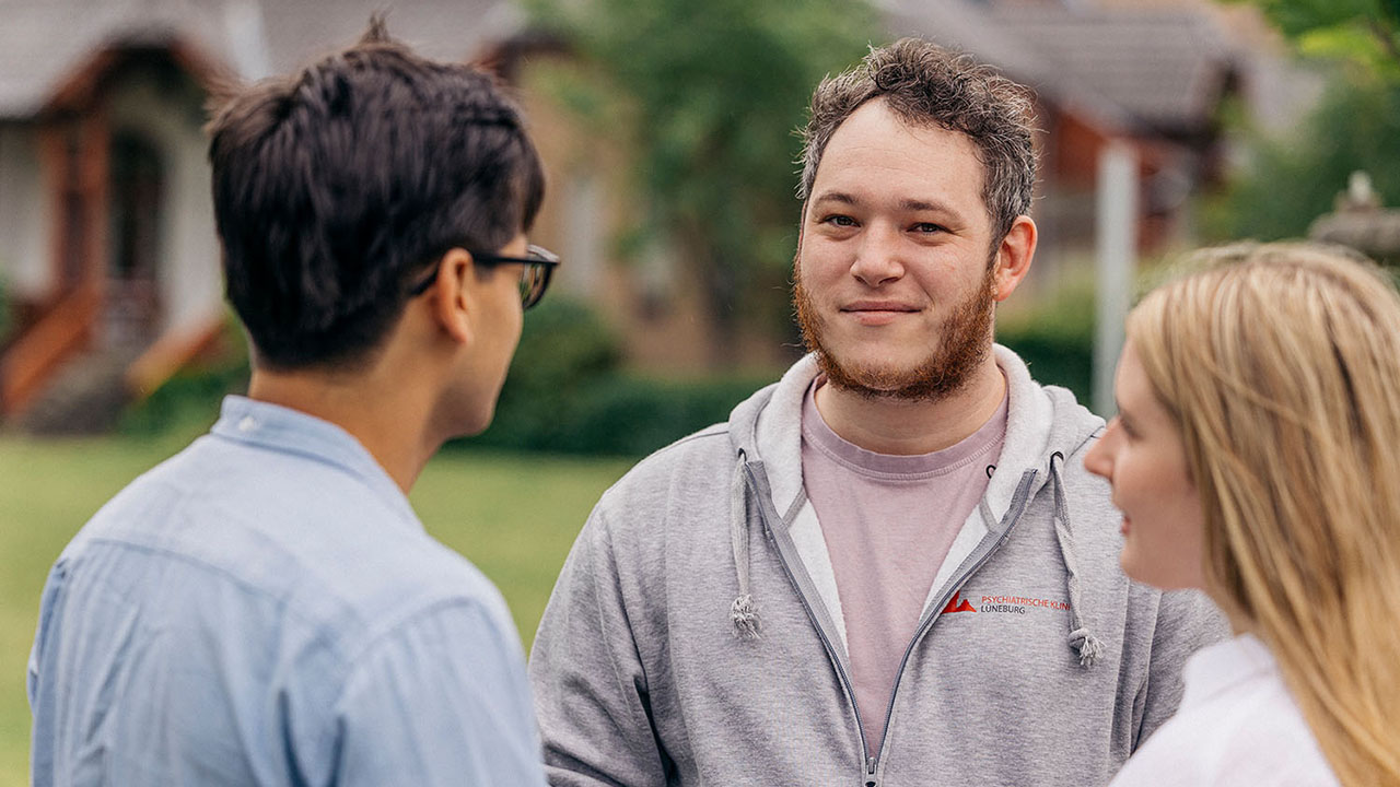Drei Personen im Gespräch, eine davon trägt eine Kapuzenjacke mit dem Logo der Klinik