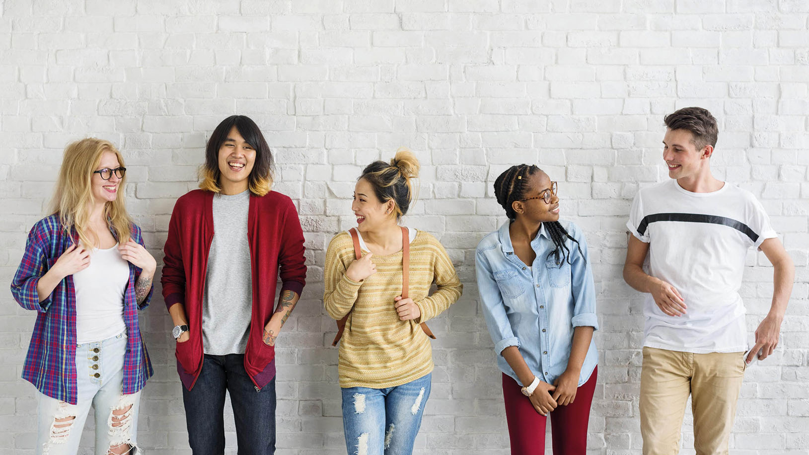Fünf junge Menschen stehen vor einer weißen Mauer und unterhalten sich gut gelaunt.