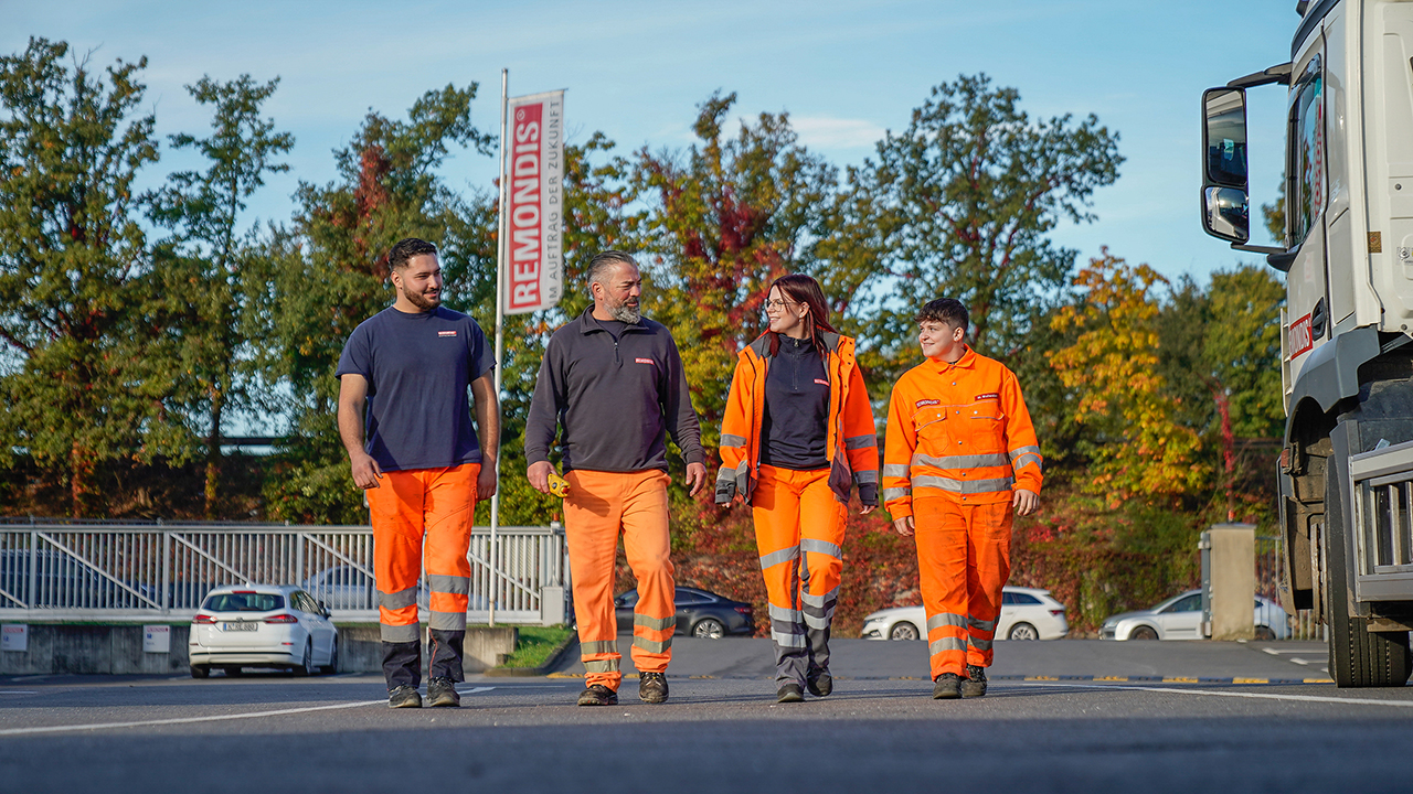 Gruppe von vier Mitarbeitenden in Arbeitskleidung läuft auf Kamera zu.