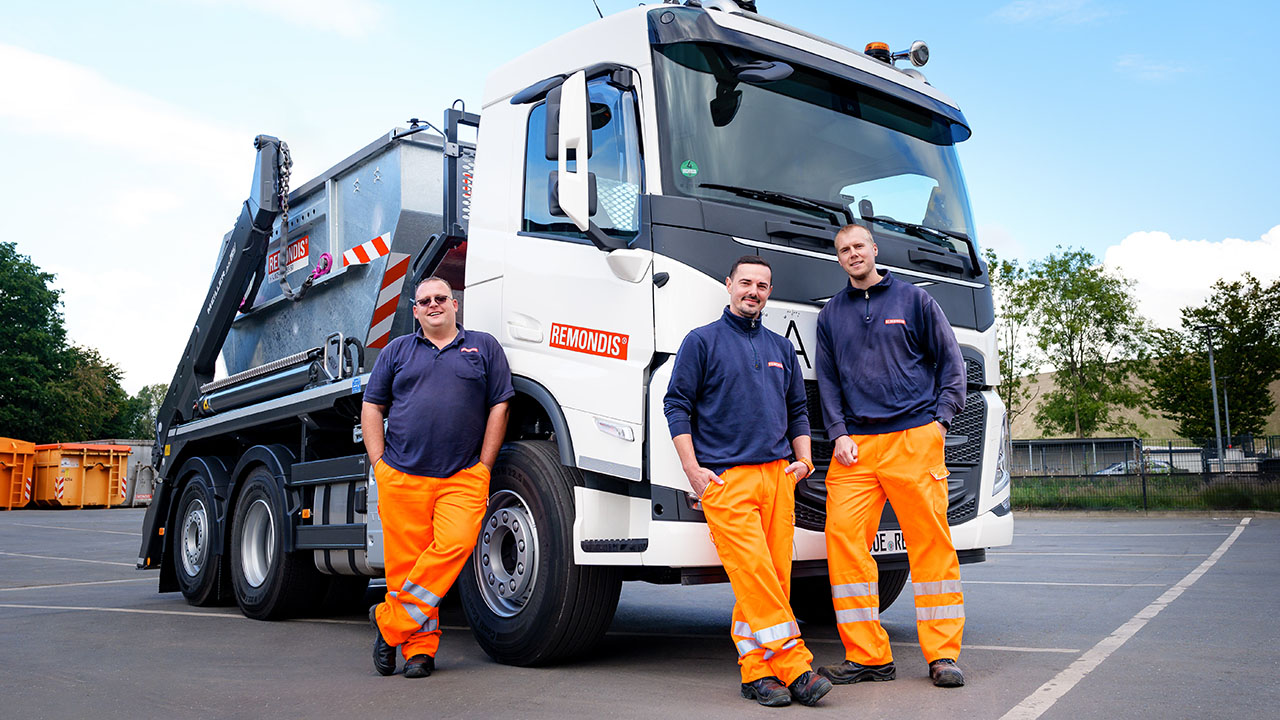 Drei Mitarbeitende in Arbeitskleidung vor einem LKW