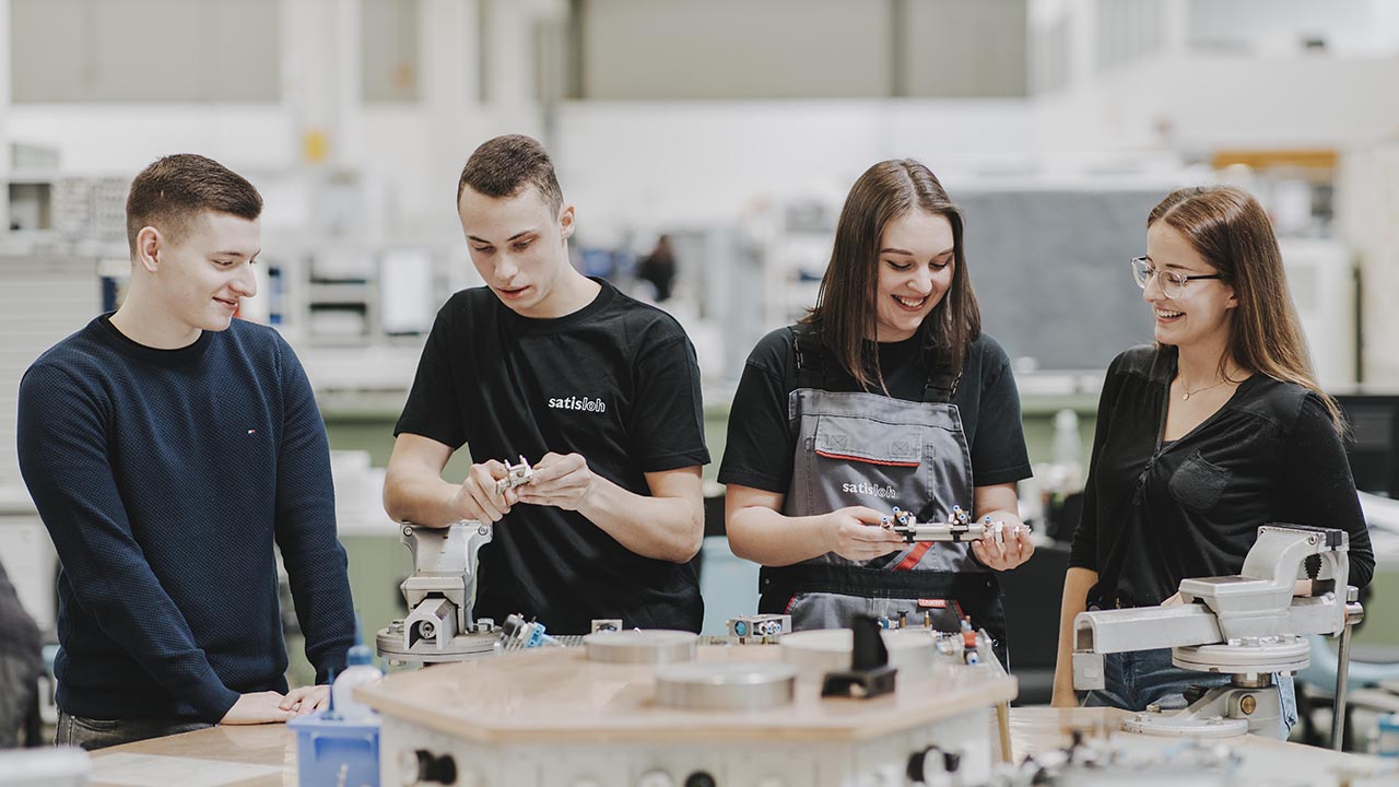 Vier Personen haben verschiedene Werkteile vor sich und lächeln.