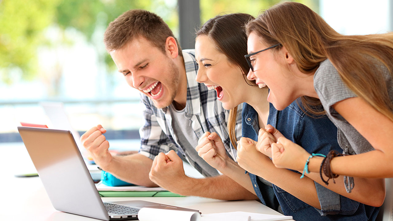 Drei junge Menschen jubeln vor Laptop