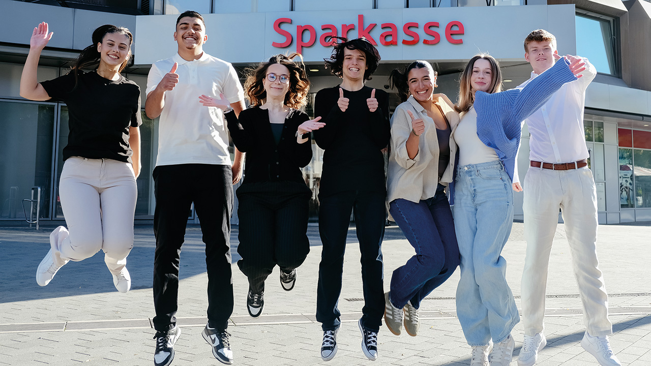 Gruppe von jungen Menschen vor der Sparkasse, springen in die Luft