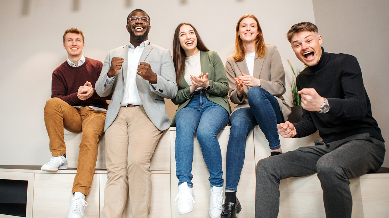 5 junge Menschen sitzen lachend nebeneinander