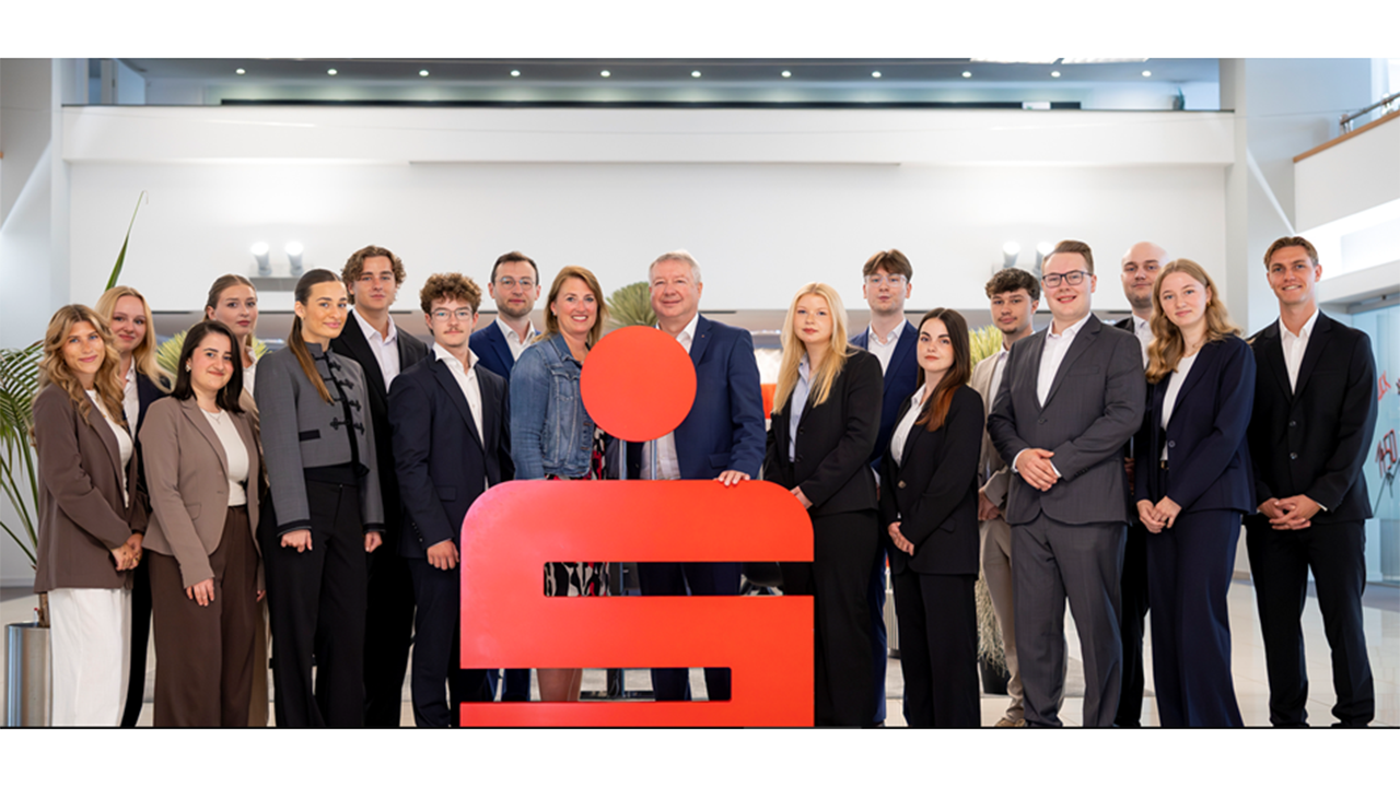 Eine Gruppe Mitarbeiter steht in Businness Kleidung im Gruppenbild vor einem grußen Sparkassenzeichen.