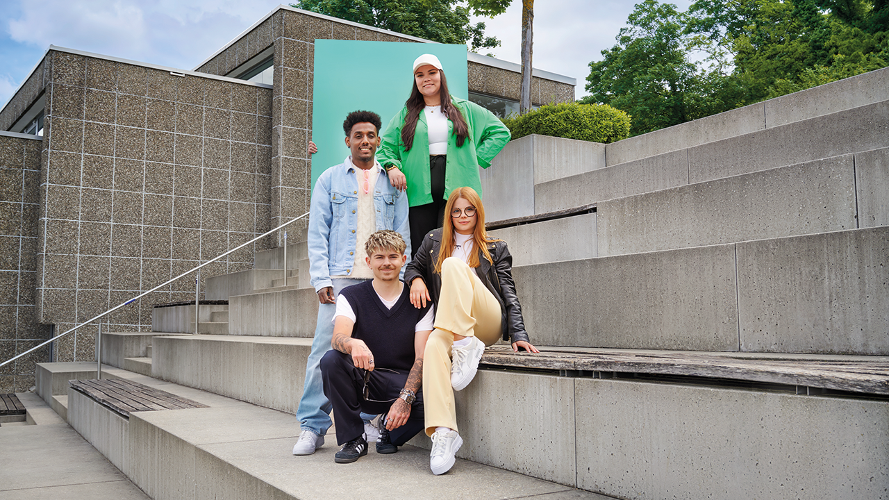 Vier Personen stehen und sitzen auf einer Treppe.