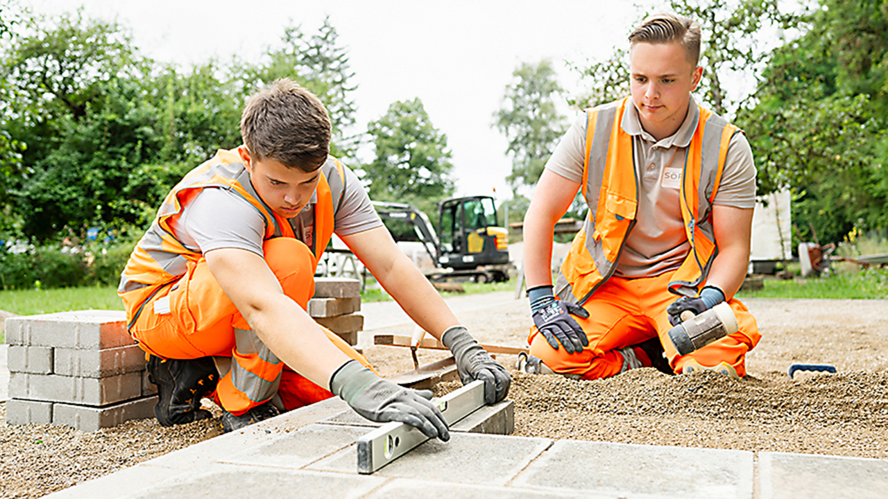 Zwei Strassenwärter-Azubis beim Verlegen von Gehwegplatten.