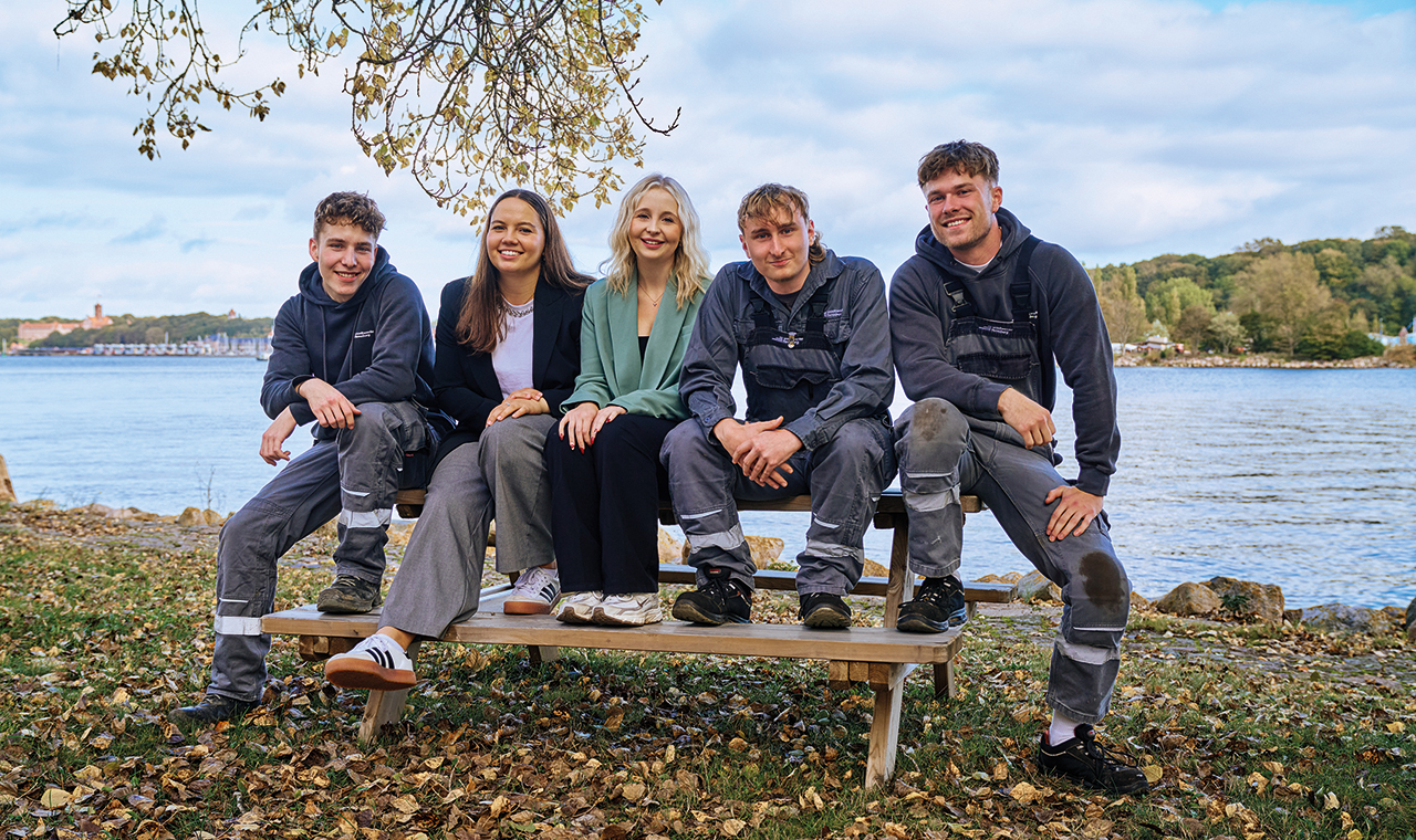 Gruppe junger Menschen auf einer Bank vor einem See im Herbst