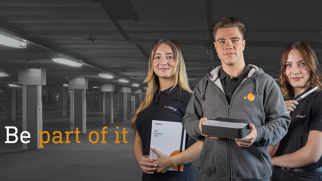 Drei Personen in der Arbeitskleidung der STEINEL GmbH. Linksseitig der Slogan "Be part of it"