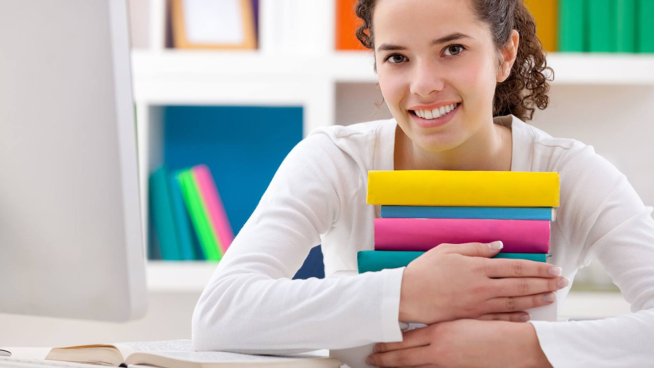 Frau hält Bücher auf dem Arm und schaut in die Kamera.