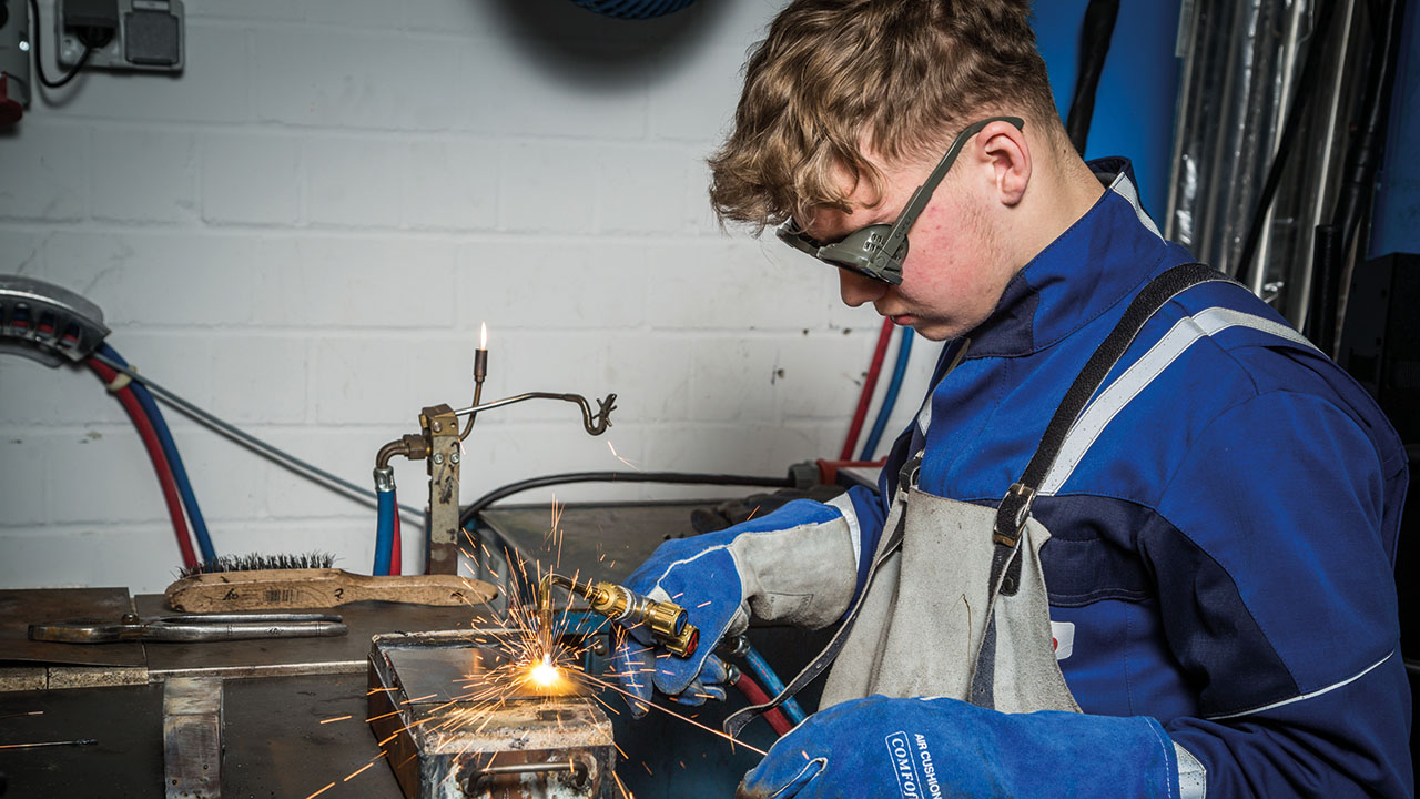 Junger Mensch in Arbeitskleidung mit Schutzbrille beim Schweißen