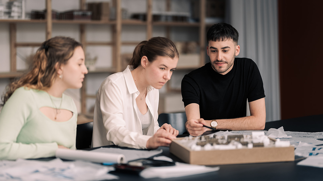 Drei Menschen sitzen am Schreibtisch und reden gemeinsam über etwas