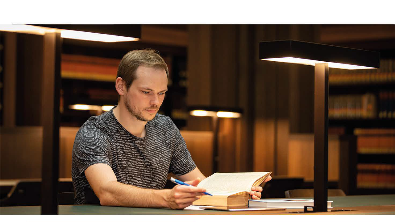 Studierender in der Bibliothek bei der Arbeit mit einem Buch.