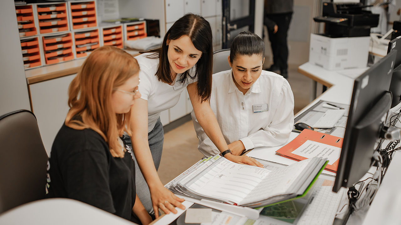 Drei junge Menschen vor dem Rechner, auf dem Tisch ein Aktenordner