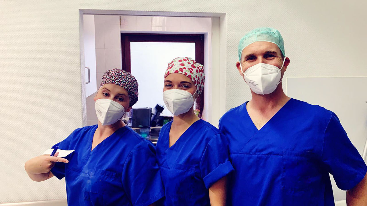 Drei Personen in blauer Arbeitskleidung mit Mundschutz und Haube