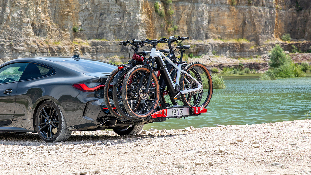 Ein Auto mit einem Fahrradanhänger steht an einem Ufer im Hintergrund sieht man Felsen.