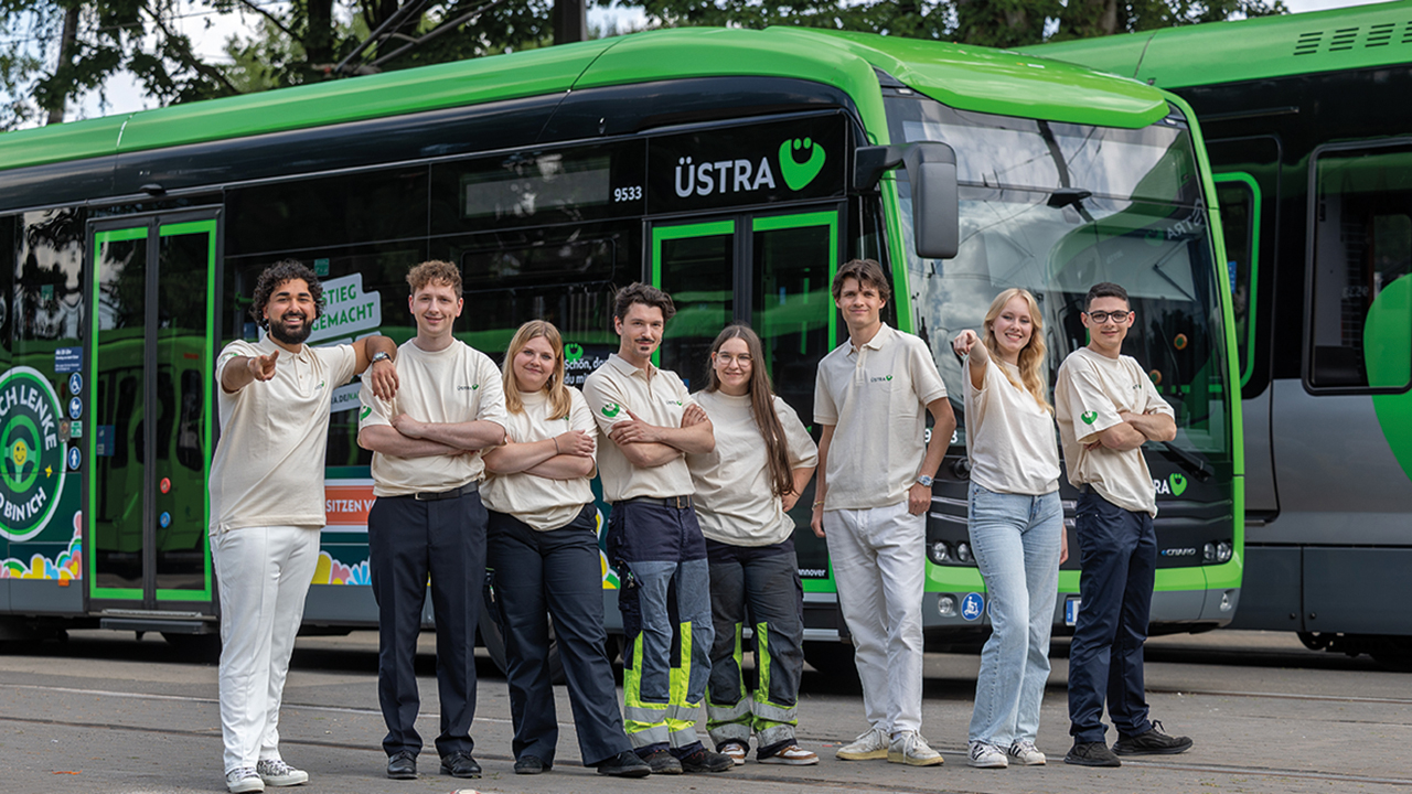 Azubis die fröhlich vor einem ÜSTRA Bus stehen