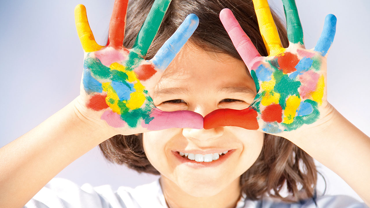 Lachendes Kind hält bunt bemalte Hände in die Kamera