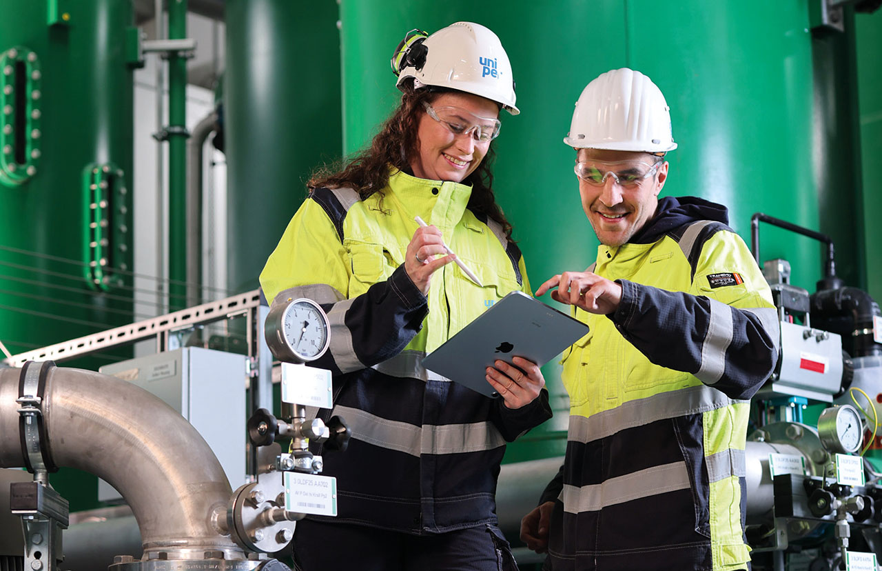 Zwei Angestellte in neongelb-schwarzen Arbeitsanzügen und Helm in einer Besprechung