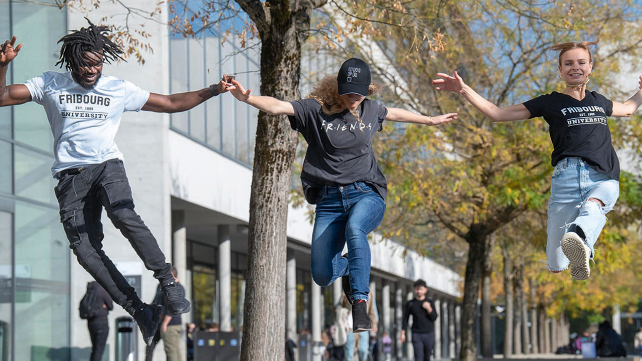 Drei Studierende springen vor dem Universitätsgebäude in die Höhe